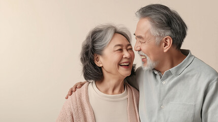 Elderly asian couple shares a heartwarming laugh together against a simple backdrop
