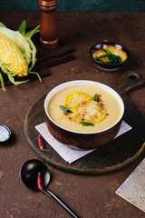 Corn soup puree in a dark bowl with corn and spice topping on a brown concrete background. Recipes corn. Seasonal products. Thanksgiving day