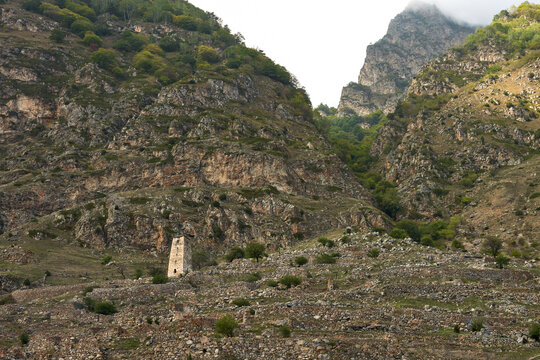 Panoramic view of an ancient watchtower with the ruins of a mountain village in the rocky mountains below the clouds.
