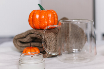 An empty glass mug, a candle in glass on the background of a folded sweater and orange pumpkins