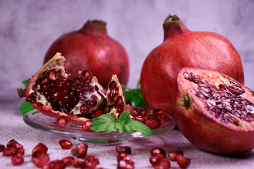 Red pomegranate on a gray background. Whole and pieces. Ripe pomegranate seeds on a glass plate. All mint leaves.