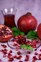 Red pomegranate on a gray background. Whole and pieces. Ripe pomegranate seeds on a glass plate. All mint leaves.