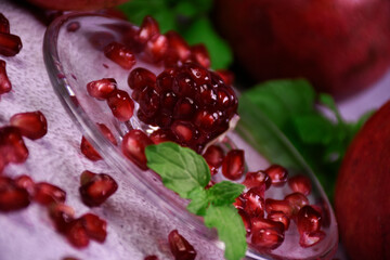 Red pomegranate on a gray background. Whole and pieces. Ripe pomegranate seeds on a glass plate. All mint leaves.
