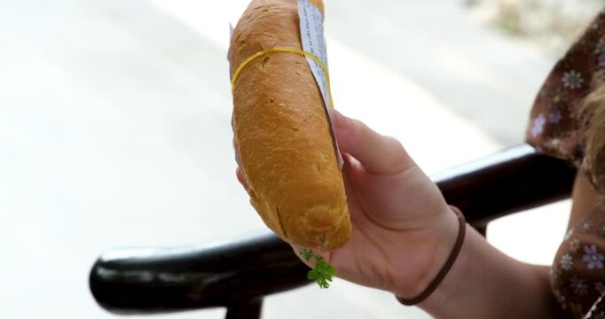 Vietnamese traditional bun with filling in hands of European girl tourist wrapped in a piece of paper with elastic band tasting local food girl woman bites bun tasty cheap