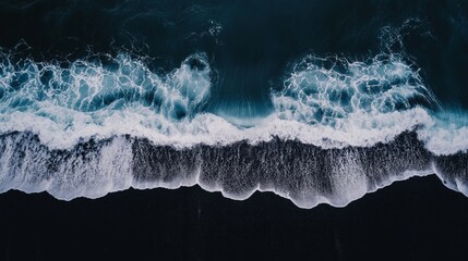 Fototapeta premium a teal and blue sapphire wave crashes onto a dark, black sandy beach, captured from a bird's eye view.