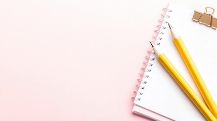 Two pencils and a notebook resting on a pink desk with copy space