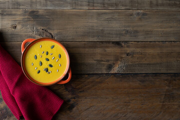 A bowl of soup with seeds on top of a wooden table. The bowl is orange and the table is brown