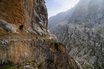 A mountain range with a rocky cliff and a cave. The mountain range is covered in rocks and the cave is located on the side of the cliff. The scene is serene and peaceful