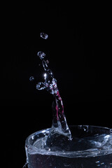 Water droplets splash high from a glass container against a dark background during a creative photography session