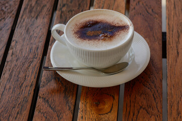A warm cup of frothy coffee rests on a wooden table, inviting cozy conversations and delightful moments on a sunny afternoon