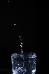 Water droplets splash upward from a clear glass in a dark setting, revealing dynamic motion and energy during nighttime