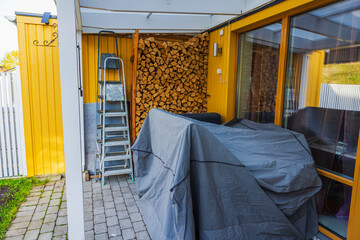 Winter preparation at villa with stacked firewood and covered outdoor furniture. Sweden.