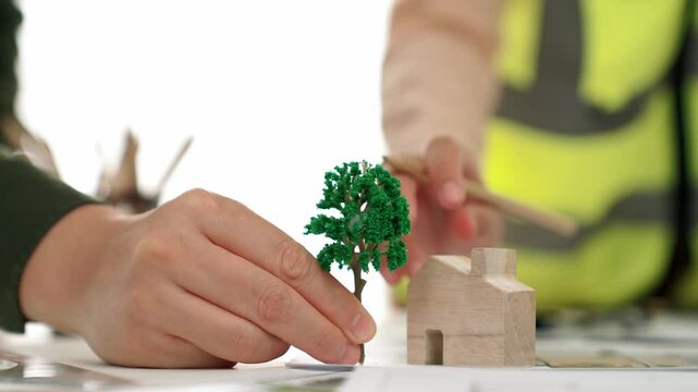 A video of architect using tree and home model to measure blueprint. Architect designing house construction on a table at studio, with architectural plan scattered around. Focus on hand. Delineation.