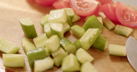 Tomatoes and cucumbers are currently being chopped on a wooden cutting board, preparing fresh ingredients for a delicious meal