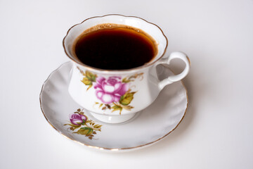 A delicate porcelain cup of coffee on a matching saucer featuring floral designs, perfect for a quiet morning