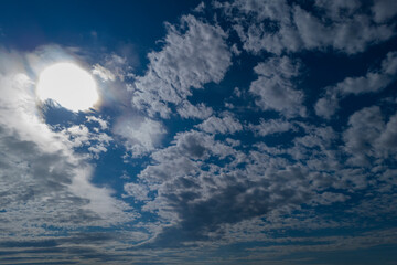 A mesmerizing view of fluffy clouds scattered across a bright blue sky with the sun shining through, creating a serene and tranquil atmosphere.