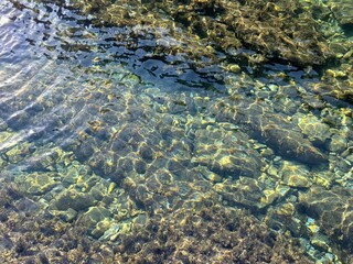 Sea water calm transparent surface with pebbles at the bottom