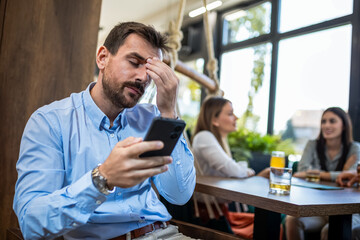 Stressed businessman using his phone in the restaurant with his friends in the backround.