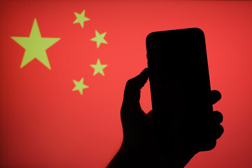 silhouette of a person holding a smartphone in front of the flag of China