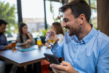 Businessman using his phone in the restaurant. Smiling and drinking beer.