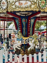 The image depicts a colorful vintage carousel featuring ornate, decorated horses. A small white picket fence surrounds the ride.