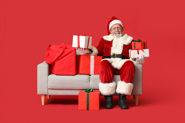 Cool Santa Claus with gift boxes sitting on sofa against red background