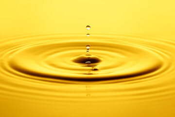 Yellow drop falling creating a splash of oil or water background. Olive, sunflower, cosmetic or motor oil