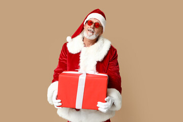Santa Claus in sunglasses with gift box on brown background