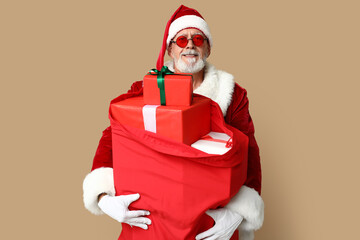 Santa Claus in sunglasses with bag full of gift boxes on brown background