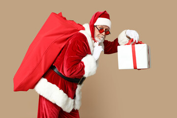 Santa Claus in sunglasses with bag full of gift boxes on brown background