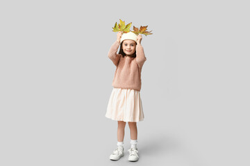 Cute little girl in stylish clothes with autumn leaves on grey background
