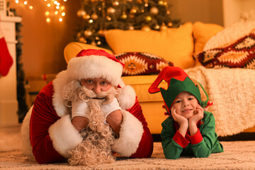 Santa Claus with cute little elf at home on Christmas eve