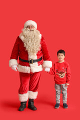 Santa Claus and cute little boy holding hands on red background