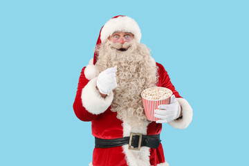 Shocked Santa Claus with tasty popcorn on blue background