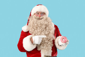 Santa Claus pointing at tasty donut on blue background