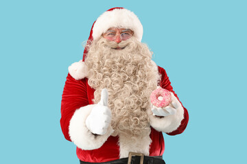 Santa Claus with tasty donut showing thumb-up on blue background