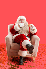Santa Claus with cup of tea and tasty burger in armchair on red background
