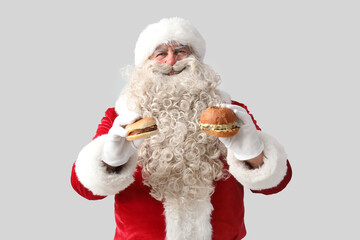 Santa Claus with tasty burgers on white background