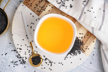 Bowl of oil with spoon and sesame seeds on white grunge background