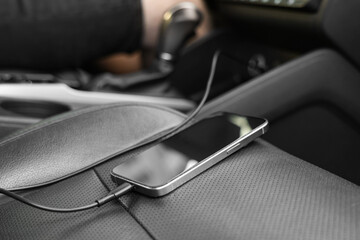 Mobile phone with charging cable on seat in car, closeup
