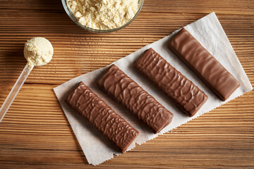 Healthy vegetarian protein chocolate bars with a scoop of whey protein powder on a wooden table