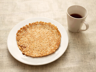 Round pancake or crepes on big plate and cup or tea or coffee on simple table cloth. Popular multi national dish.