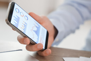 Male economist working with diagrams on mobile phone in office, closeup