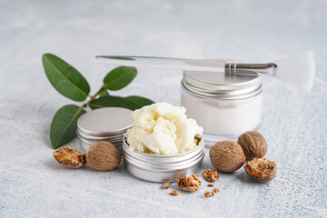 Jars of shea butter with nuts and brush on grunge background