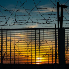 Sunset behind a barbed wire fence.