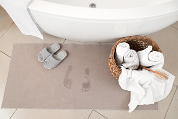 Bath mat with wet footprints, slippers and towels on floor, top view