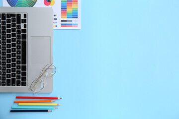Workplace of graphic designer with laptop, pencils and color charts on blue background