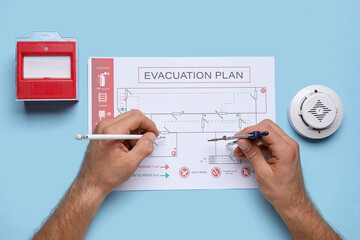Man with smoke detector and fire call point drawing evacuation plan on blue background