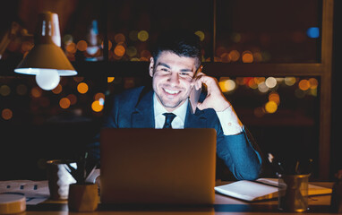 Smiling Businessman Having Phone Conversation Talking With Client Sitting At Laptop In Modern Office At Night