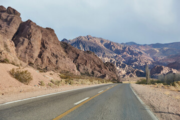 Scene of a car trip: an empty road in the middle of a rocky mountain landscape of the Andes, in Mendoza, Argentina.